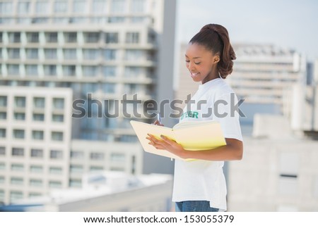 Smiling altruist woman holding notebook outdoors on urban background
