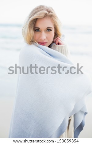 Peaceful blonde woman covering herself in a blanket on the beach