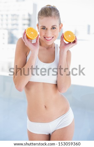 Gorgeous young blonde model in white sportswear holding two halves of an orange