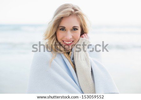 Pleased blonde woman covering herself in a blanket on the beach