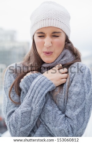 Shivering cute woman with winter clothes on posing outdoors on a cold grey day