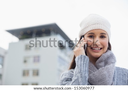 Happy gorgeous woman wearing winter clothes having a call outdoors on a cold grey day