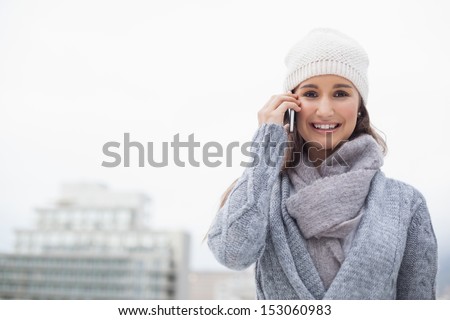 Smiling woman with winter clothes on having a call outdoors on a cold grey day