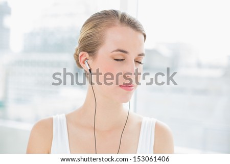 Head shot of relaxed sporty woman in bright sports hall listening to music
