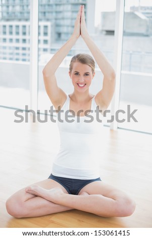 Cheerful fit woman in lotus position doing yoga session in bright sports hall