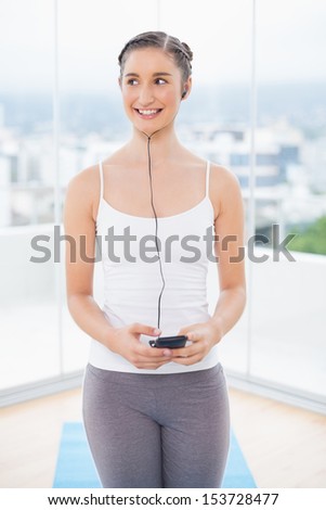 Smiling sporty model listening to music in bright fitness studio