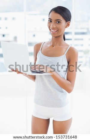 Smiling sporty model in bright room at home holding laptop