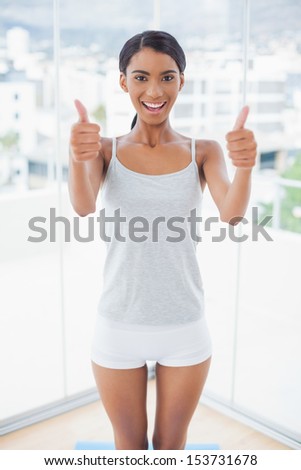 Attractive model in sportswear giving thumbs up to camera in bright room at home