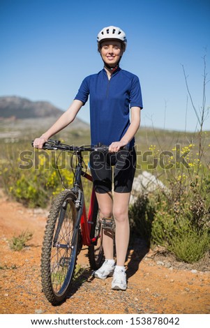 Woman standing and holding bike looking at camera on a trail in the country