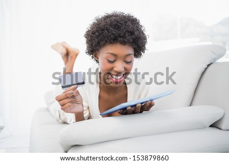 Happy pretty brunette shopping online using her tablet lying on cosy sofa