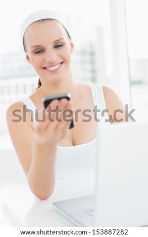 Happy pretty sportswoman looking at her mobile phone in a bright room