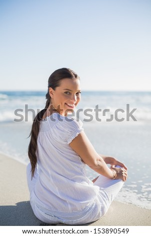 Rear view of smiling woman on the beach on a sunny day looking over shoulder at camera