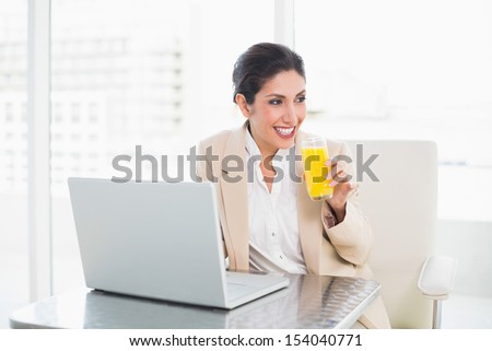 Smiling businesswoman with laptop and glass of orange juice at desk at the office