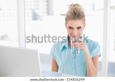 Smiling well dressed businesswoman drinking water in bright office