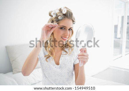 Smiling natural blonde using tweezers on her eyebrow sitting on cosy bed