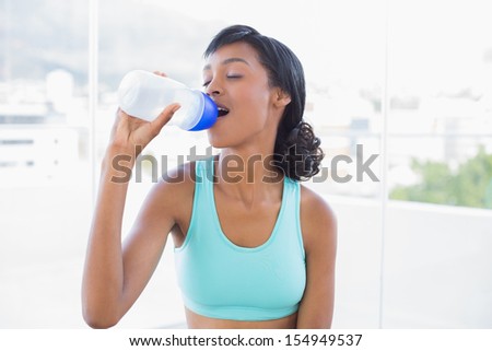 Attractive fit woman drinking a bottle of water in a living room