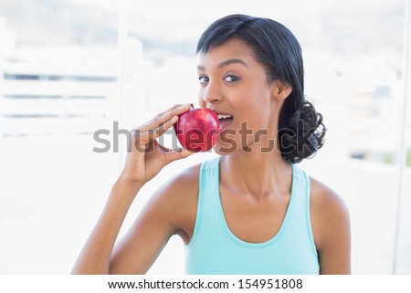 Charming black haired woman eating an apple in a living room