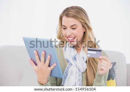 Happy pretty blonde in bright living room using her credit card to buy online
