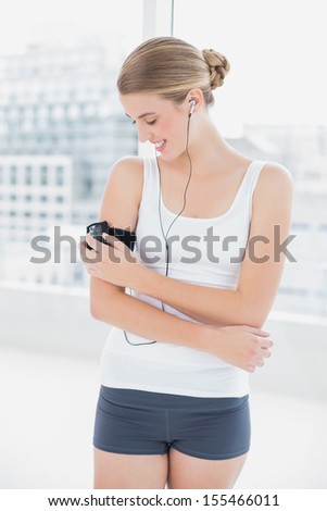 Happy sporty woman in bright sports hall changing song on her mp3