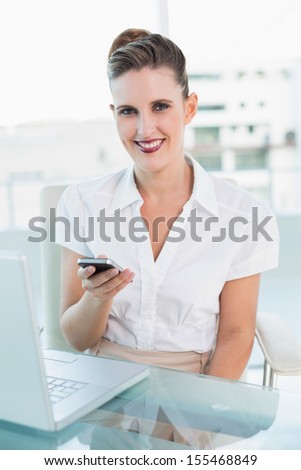 Cheerful attractive businesswoman using phone in bright office