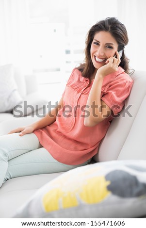 Pretty brunette sitting on her sofa on the phone at home in the living room