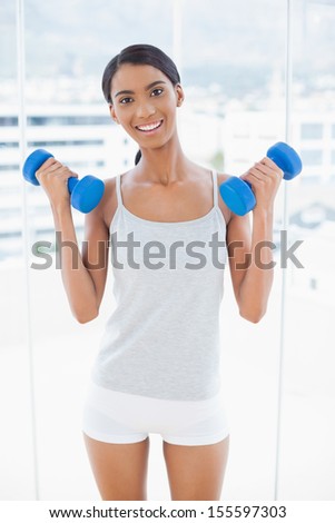 Happy sporty model exercising with dumbbells in bright room at home