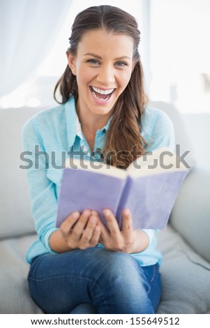 Smiling woman sitting on couch in bright living room holding book
