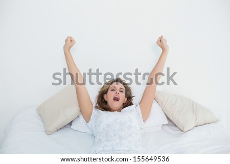 Pretty blonde woman stretching in bed and yawning in bedroom at home