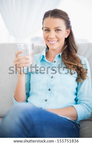 Gorgeous casual woman on couch holding glass of water looking at camera