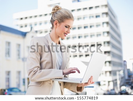 Smiling gorgeous businesswoman working on laptop outdoors on urban background