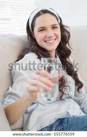 Gorgeous casual woman on cosy couch in bright living room holding water