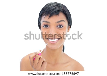 Joyful black haired woman applying gloss on her lips on white background