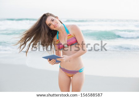 Attractive slim brown haired model in colored bikini holding a tablet pc on the beach