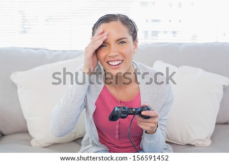 Irritated pretty woman sitting on sofa in bright living room playing video games