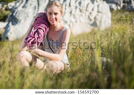 Blonde woman holding climbing equipment crouching down looking at camera