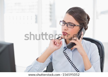Confused classy brown haired businesswoman answering the telephone in bright office