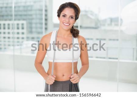 Sporty smiling brunette holding skipping rope in bright room