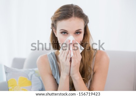 Sick young woman sitting on sofa blowing her nose at home in the sitting room