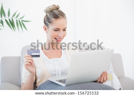 Smiling fresh model shopping online using laptop sitting on cosy sofa