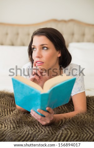 Thoughtful pretty brown haired woman holding a book in a chic bedroom