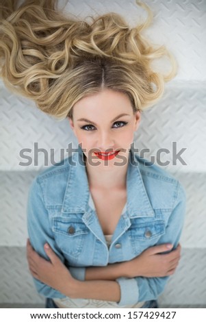 Smiling blonde wearing denim clothes lying on stairs looking at camera