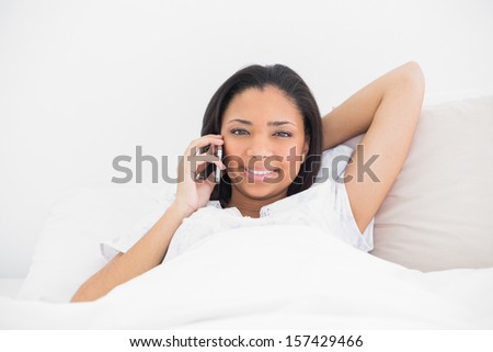Relaxed young dark haired model making a phone call in bright bedroom