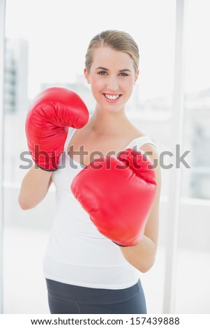 Smiling fit woman with red gloves boxing in bright sports hall
