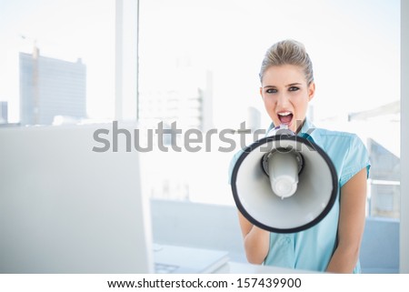 Angry elegant woman shouting in megaphone in bright office