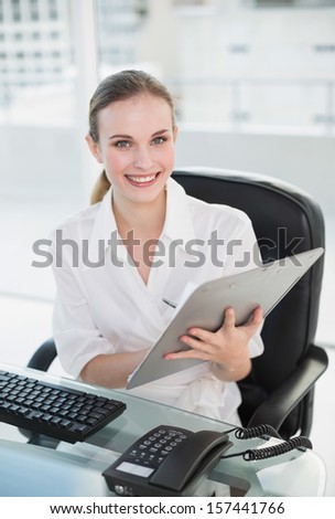Happy businesswoman writing on clipboard sitting at desk in her office