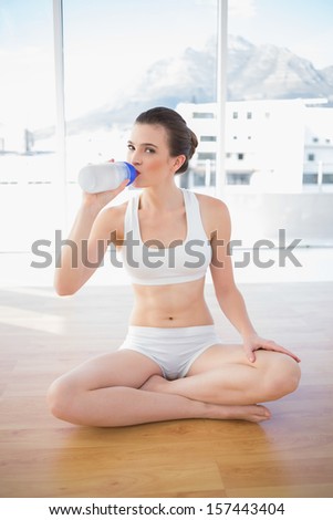 Thoughtful fit brown haired model in sportswear drinking water in bright fitness studio