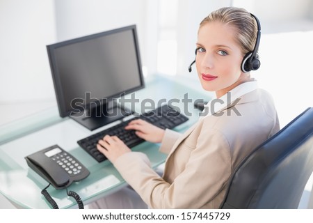 Blonde call center agent typing looking at camera in bright office