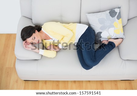Peaceful casual brunette in yellow cardigan sleeping on the couch in bright  living room