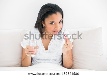 Pretty young dark haired model taking medication in bright bedroom