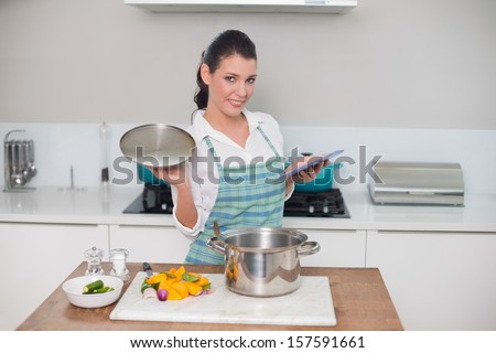 Happy gorgeous woman wearing apron using tablet while cooking in bright kitchen